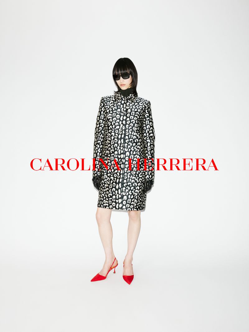 Model wearing a black and white patterned coat, dark sunglasses, and red shoes against a plain white background with red brand text.