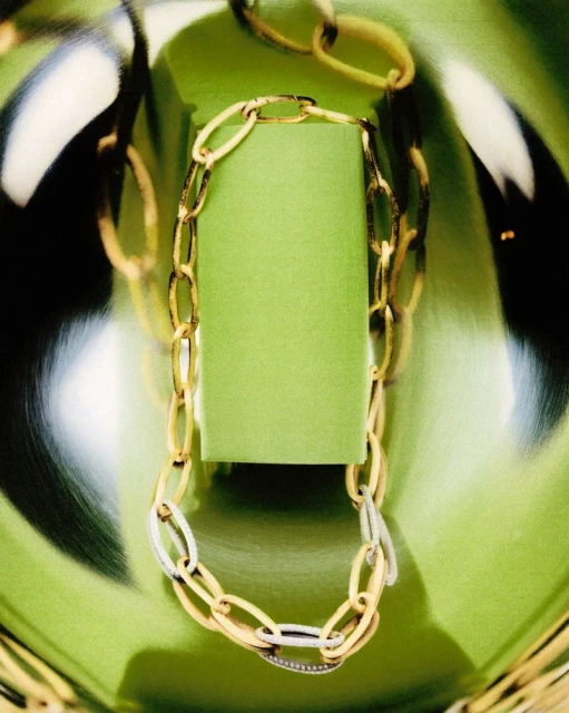 Gold and silver chain necklace on a light green box, displayed on a reflective, light green surface. Jewelry product shot.