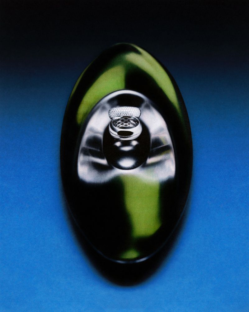 Close-up studio shot of a glossy dark green perfume bottle with silver accents against a gradient dark blue backdrop, product photography.