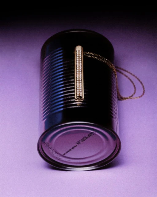 Gold necklace with rectangular pendant on a black tin can set against a blended gradient of purple and violet background.