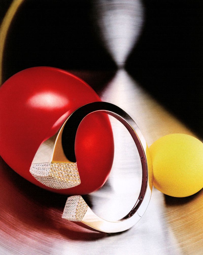 Modern metal and diamond bracelet with red and yellow spheres creates a bold and luxurious still-life jewelry shot on a textured surface.