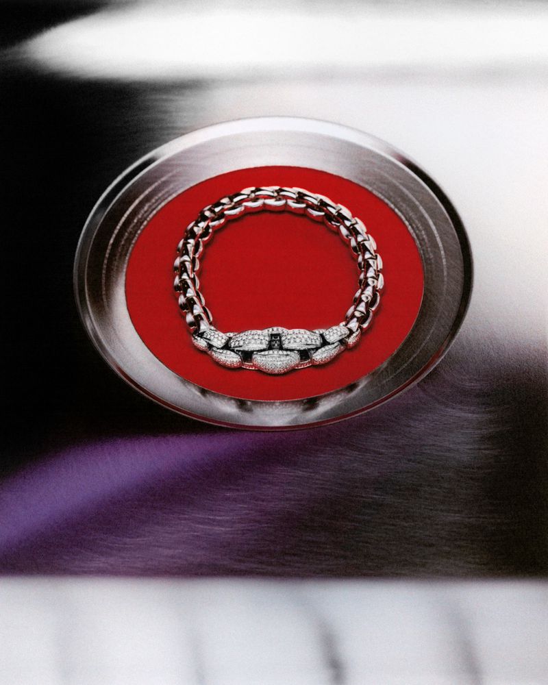 A silver and diamond necklace is centered on a round, red surface surrounded by a brushed metal texture with purple undertones.