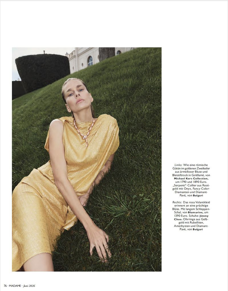 Model in a gold dress lying on a sloping grassy hill wearing a statement necklace