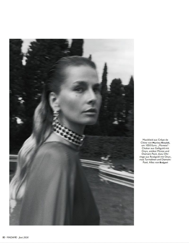 Black and white portrait of a woman wearing a statement choker necklace outdoors in a garden setting.
