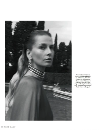 Black and white portrait of a woman wearing a statement choker necklace outdoors in a garden setting.