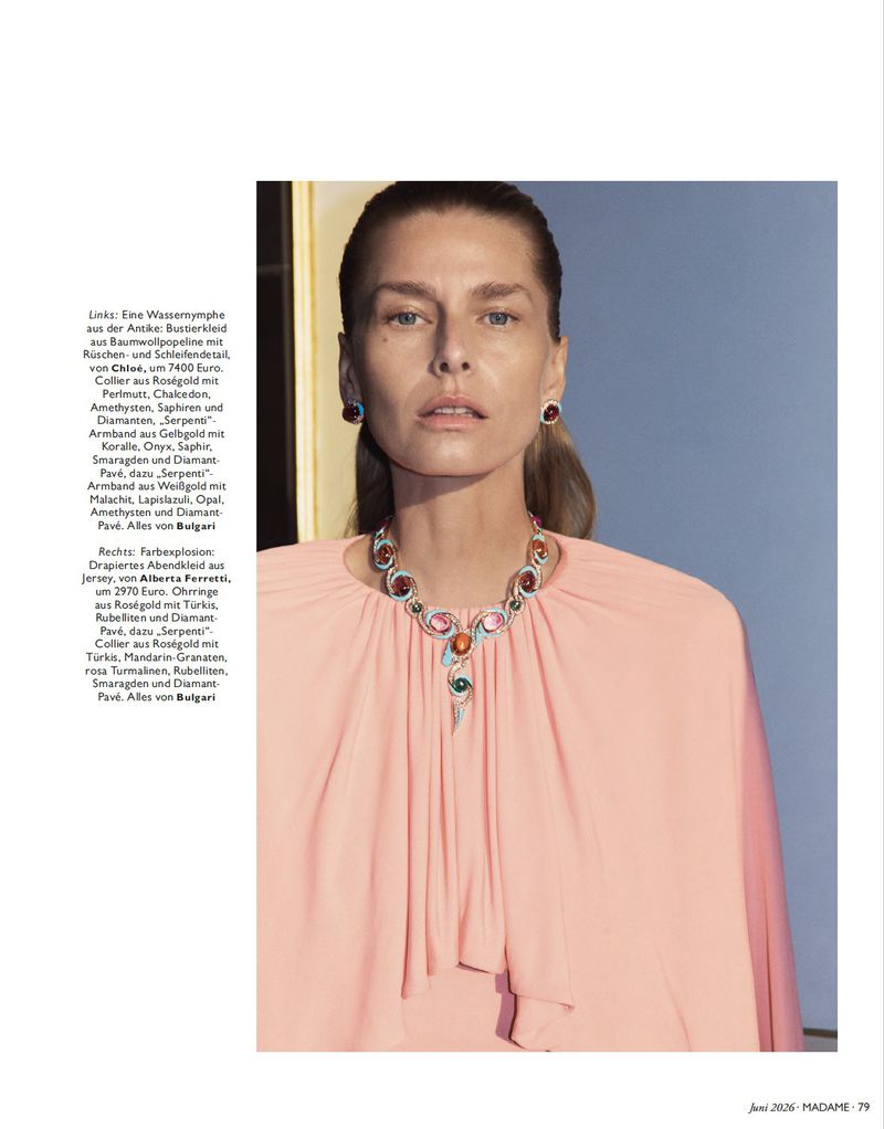 Model wearing a peach top and intricate gemstone necklace with matching earrings against a blue background