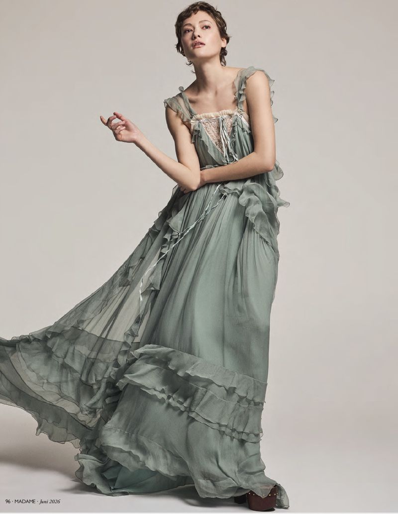 Model Daria Zolotova wearing a ruffled sage green maxi dress against a plain grey studio backdrop