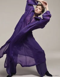 Model in a long sheer purple coat with hands raised in a dynamic pose against a neutral studio backdrop