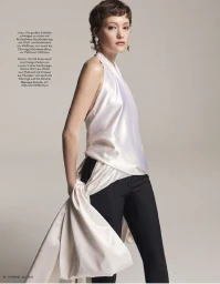 Model with short brown hair wearing a white silk halter top and dark trousers against a plain neutral background.