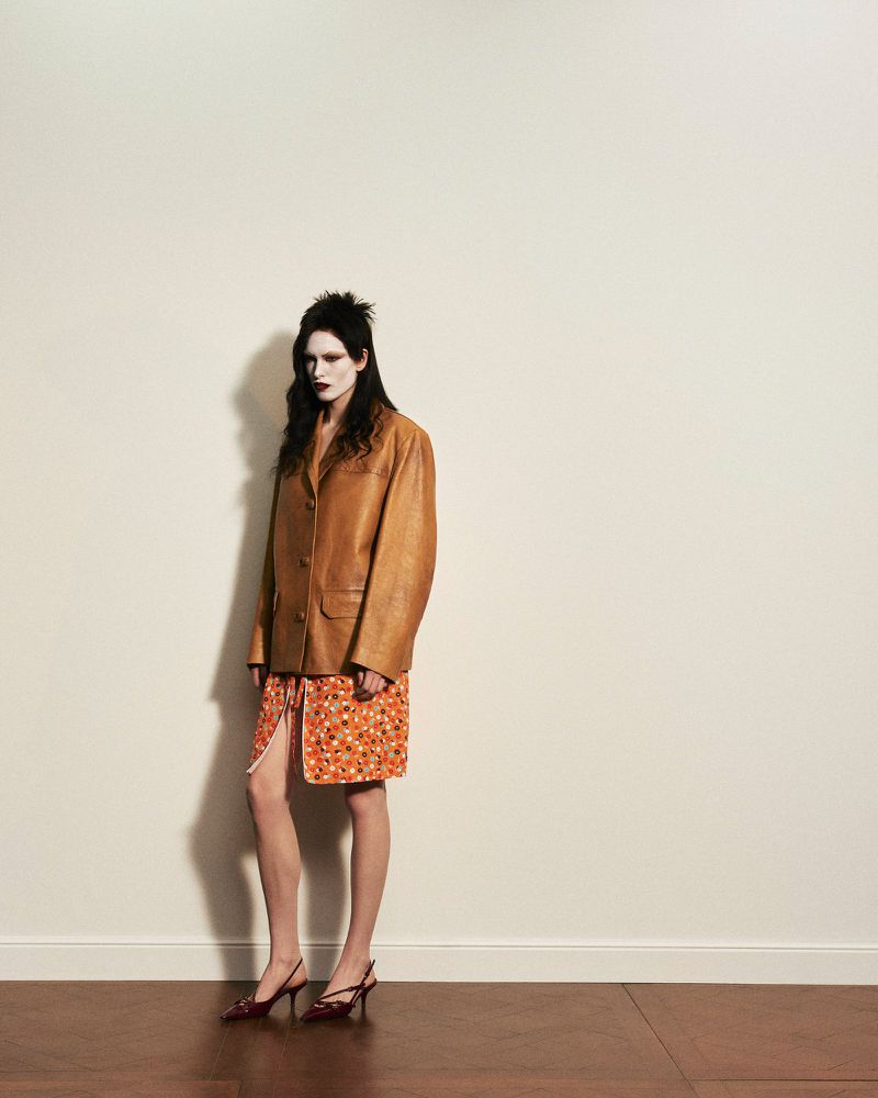 Model wearing a brown leather jacket and patterned skirt standing against a plain off-white wall for Numero Istanbul Persona.