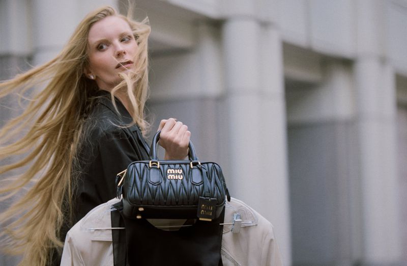 Blonde model holding a black quilted handbag outdoors in front of a stone building exterior for Numéro Istanbul