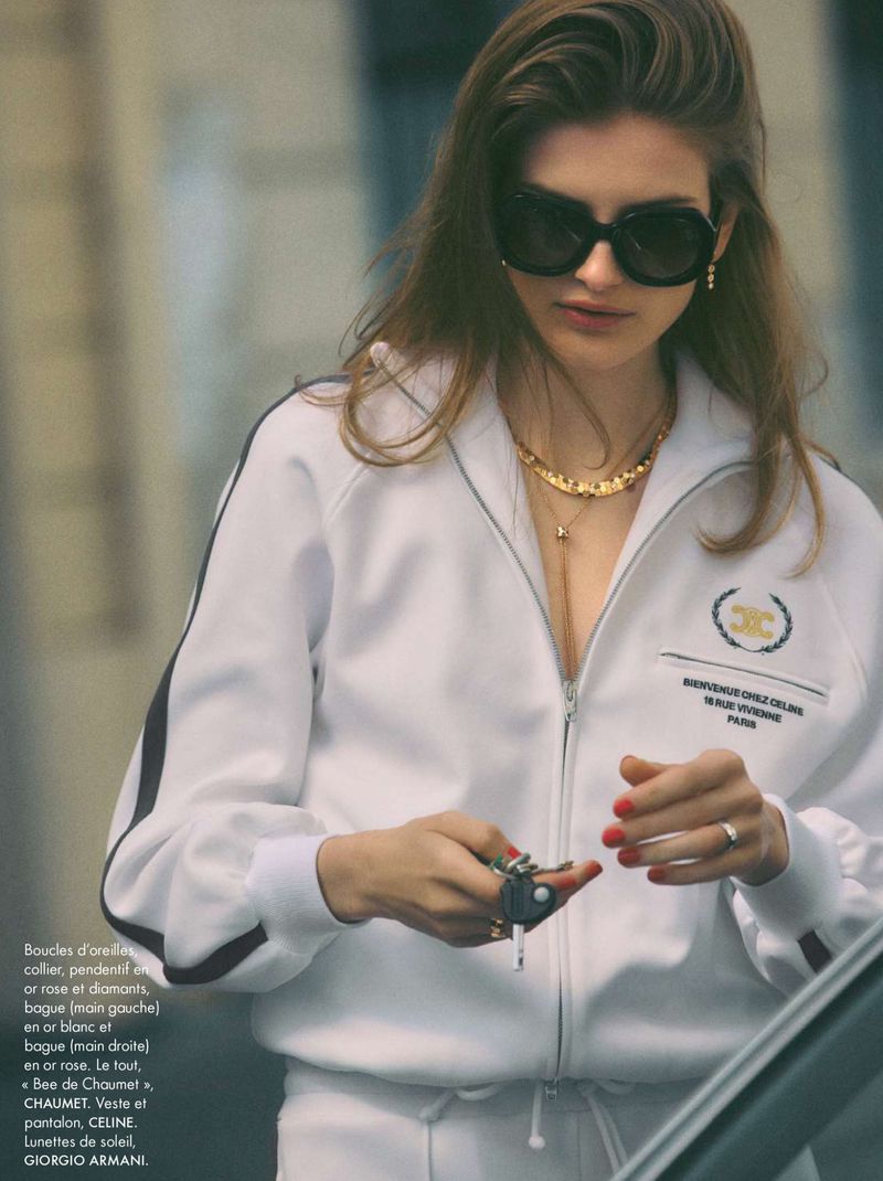Model wearing dark sunglasses and a white zip-up jacket holding keys outdoors.