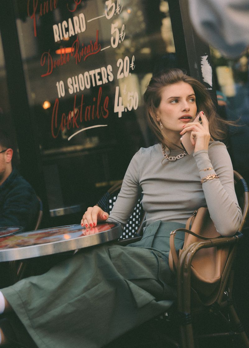 Woman sitting at an outdoor cafe table talking on a mobile phone for an Elle France fashion editorial