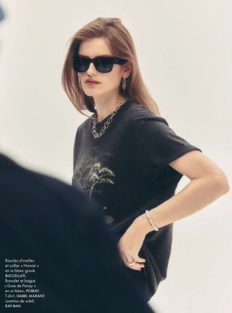 Model wearing dark sunglasses, black graphic t-shirt, and silver jewelry against a white background