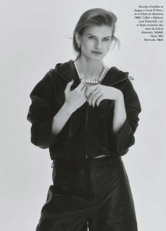 Model wearing a black zip-up jacket and pearl necklace against a seamless white background in black and white.