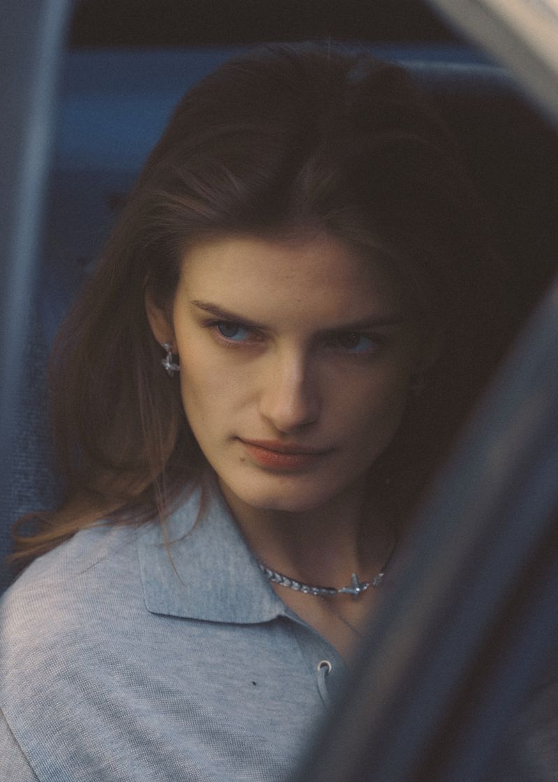 Close-up of a model wearing a grey polo shirt looking out from inside a car