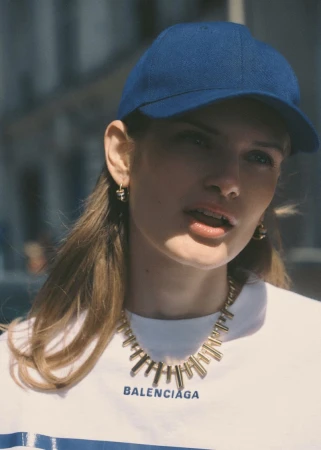 Model wearing a blue baseball cap and gold necklace with a white t-shirt for Elle France.