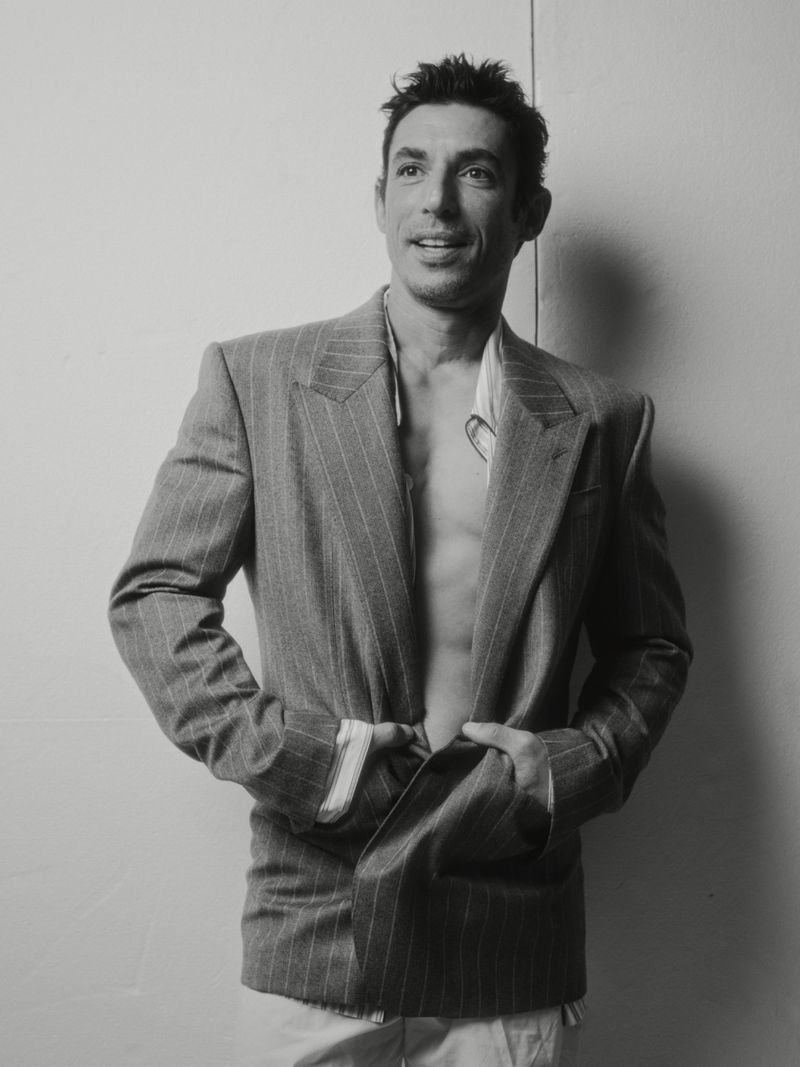 Portrait of actor Alberto Guerra wearing an open pinstripe blazer against a plain white studio background.