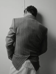 Man wearing a structured pinstripe suit jacket viewed from the back against a pale studio wall