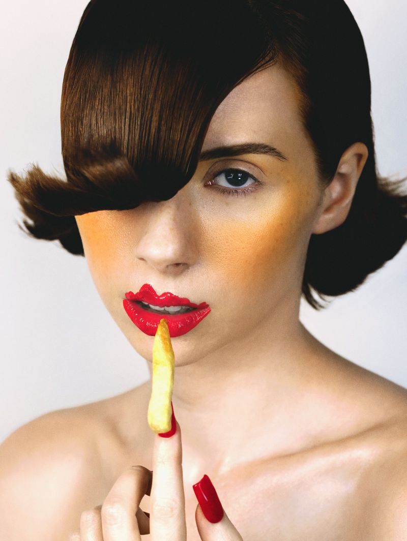 Close-up portrait of a woman with red lipstick holding a french fry against a plain white background for Vanity Teen Magazine.