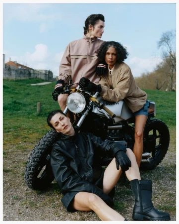 Three models posing with a vintage motorcycle outdoors on a grassy slope for Family Style Pressure Release editorial.