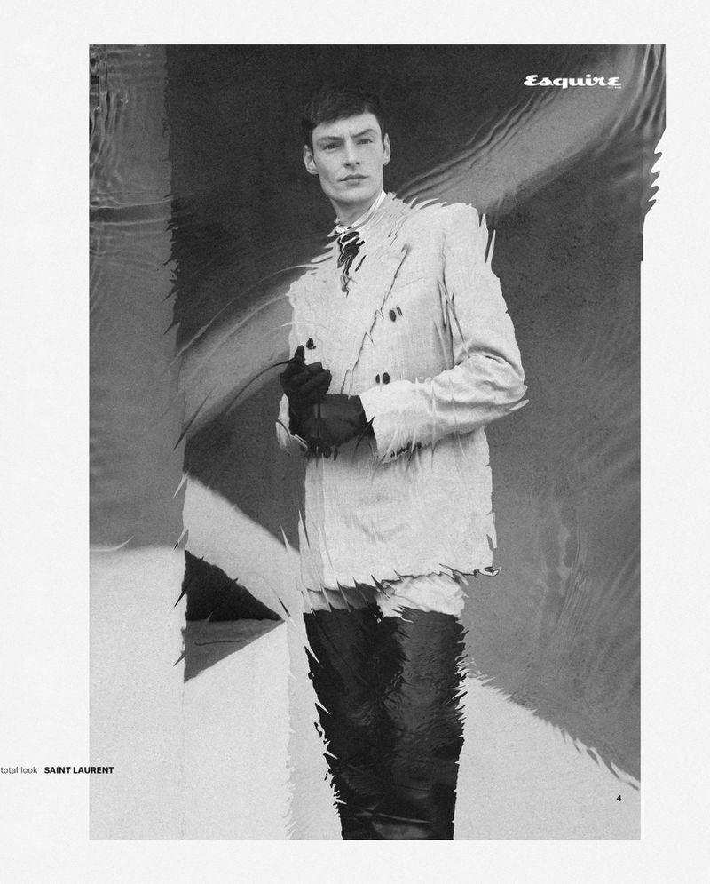 Black and white editorial fashion portrait of a male model in a textured double breasted jacket and dark gloves.