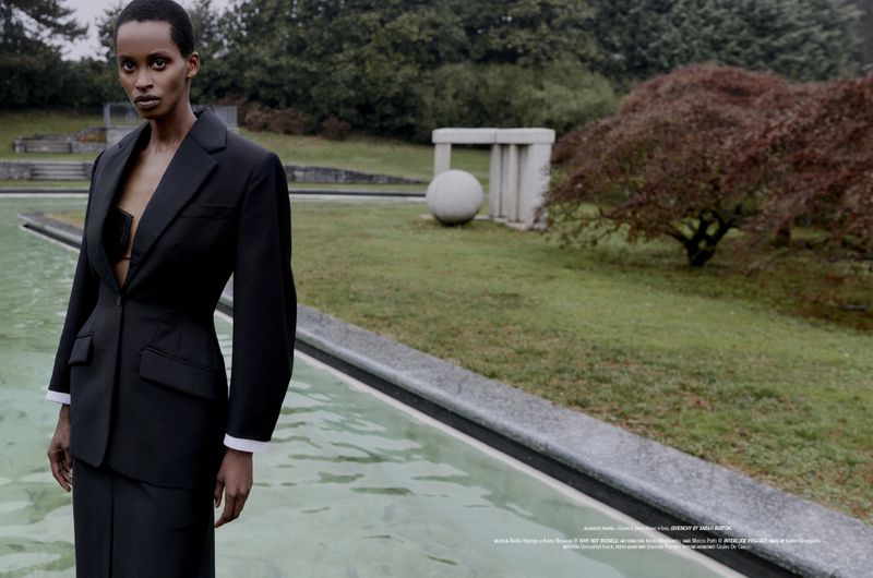 Model in a black tailored suit standing by a reflecting pool in a park for L'Officiel Italia editorial.