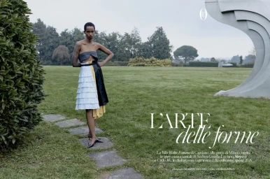 Model standing on stone path in a green park wearing a strapless top and pleated white skirt for editorial shoot