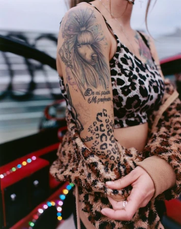 Close-up of a tattooed woman wearing a leopard print top and jacket with a fuzzy collar against an out-of-focus background.