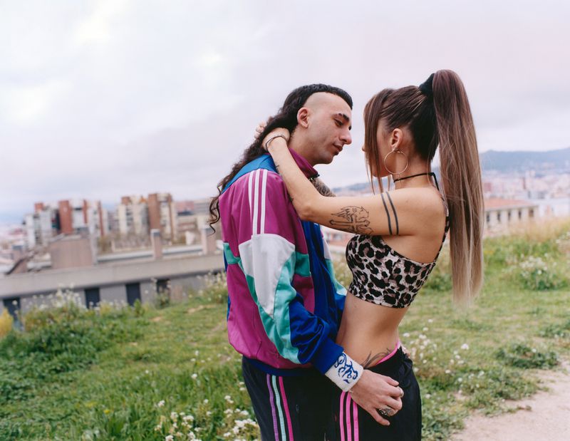 Young couple embracing outdoors with a city skyline and buildings visible in the background.