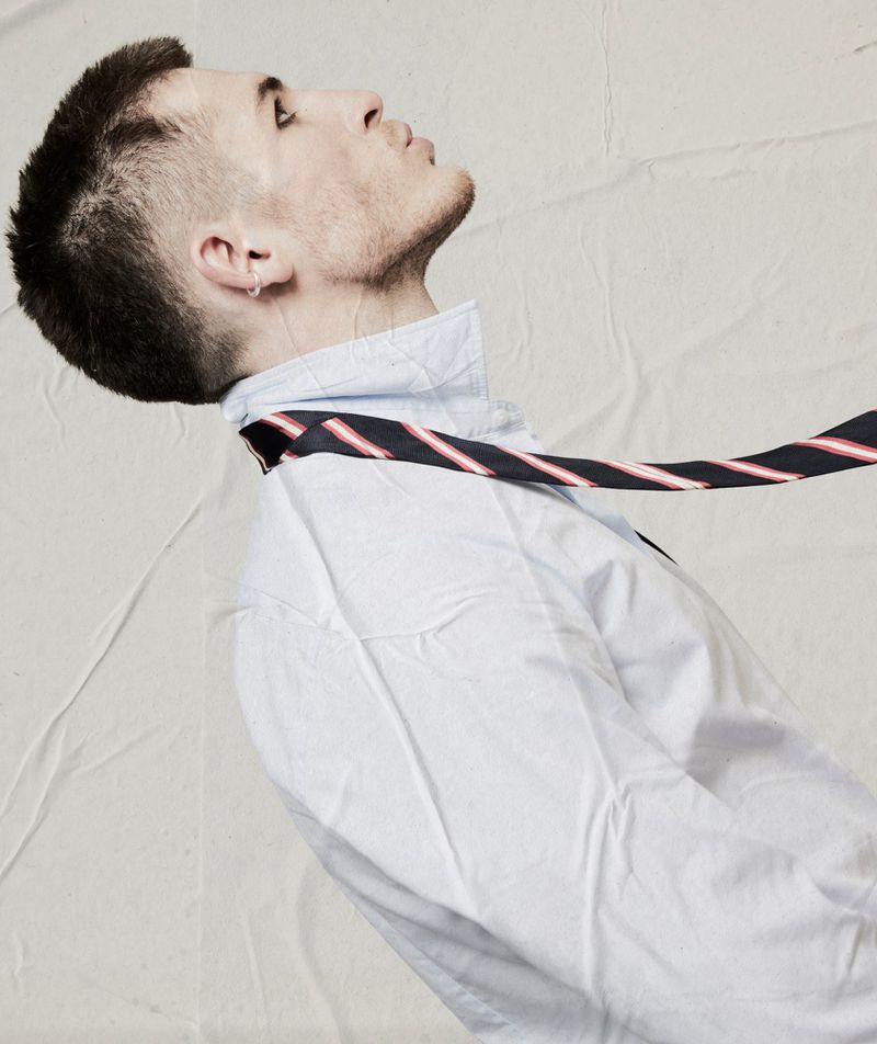 Profile portrait of a man in a white collared shirt with a striped tie against a neutral textured background