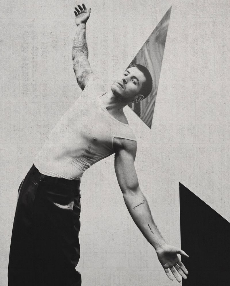 Black and white portrait of a man in a light tank top and dark trousers posing against a geometric textured background