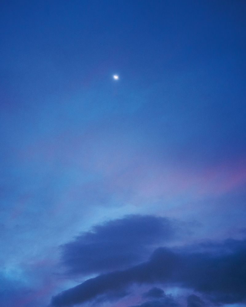 Scenic night sky featuring a vibrant gradient of blue hues, wispy clouds, and a softly glowing moon, creating a serene and atmospheric vista.