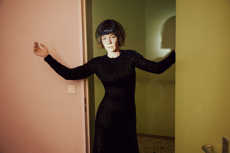 Sandra Hüller wearing a black evening gown and veiled hat standing in a doorway