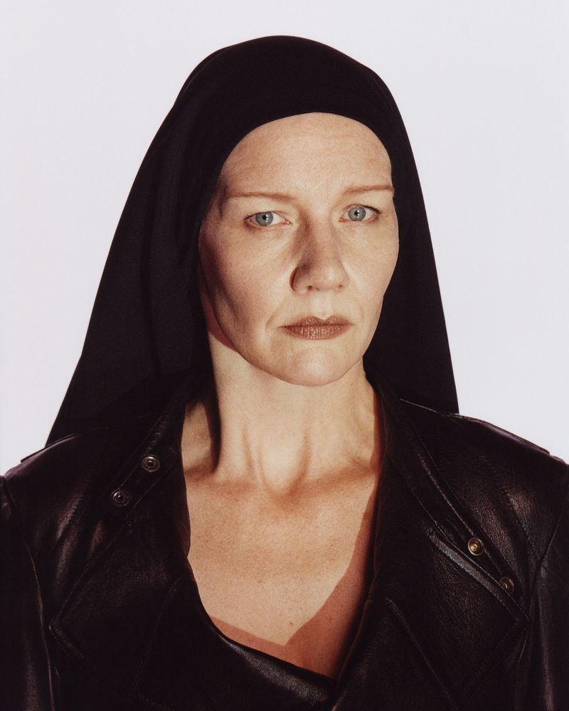 Portrait of Sandra Hüller wearing a black leather jacket and head covering against a white background