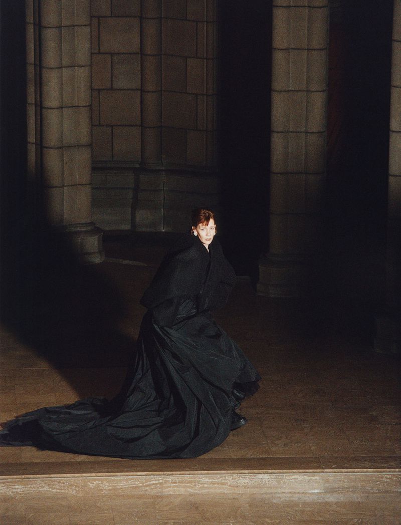 Sandra Hüller wearing a long black coat in a dimly lit stone interior by Harley Weir for Family Style