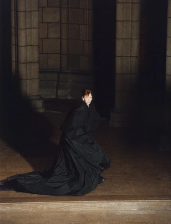 Sandra Hüller wearing a long black coat in a dimly lit stone interior by Harley Weir for Family Style