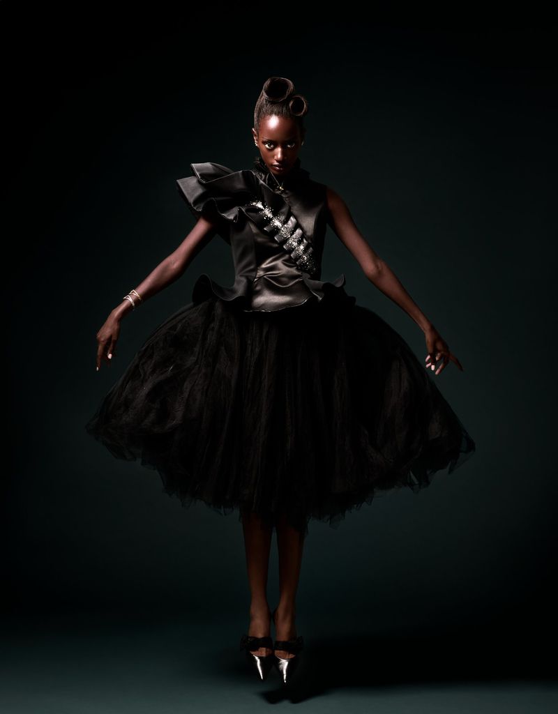 Model floating in mid-air wearing a sculptural black ruffled satin dress with a voluminous tulle skirt against a dark background.