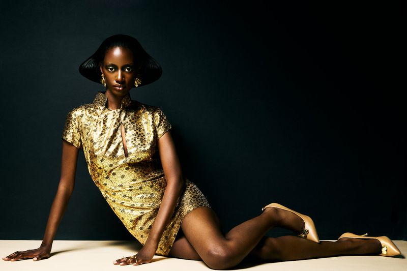 Elegant woman in a gold sequin dress poses in a studio setting with a dark background, radiating confidence and style in a fashion shot.