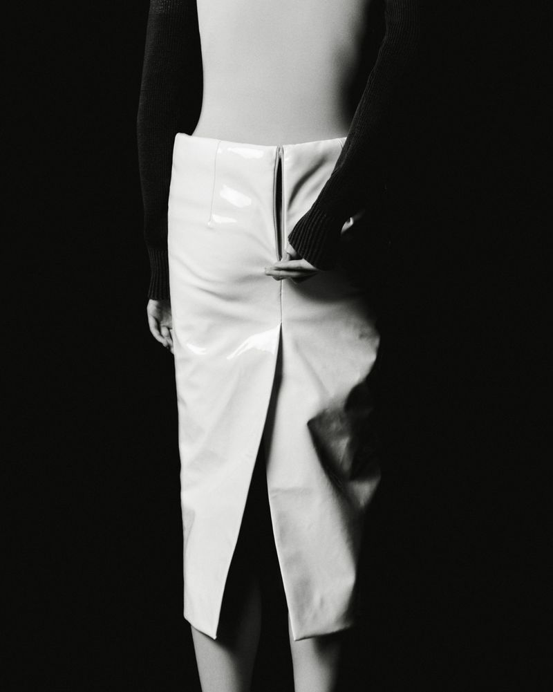 Model wearing a white glossy skirt and black top against a solid dark background for The Travel Almanac.