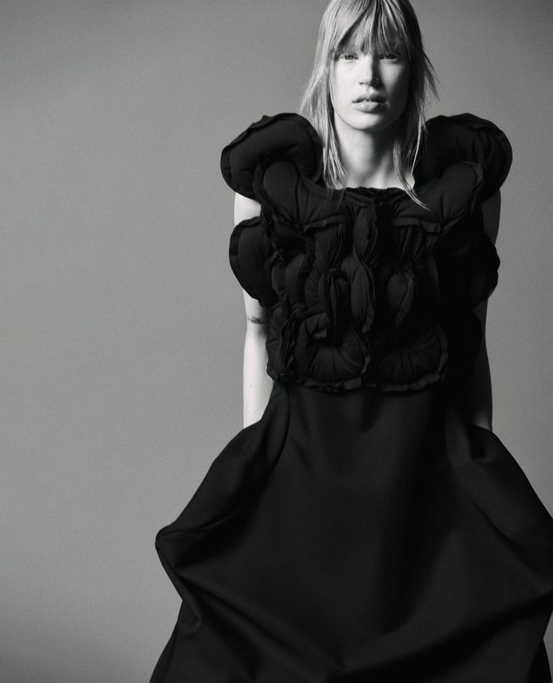 Monochrome portrait of a woman wearing a black dress with puffed sleeves, posing against a neutral gray background in a studio setting.