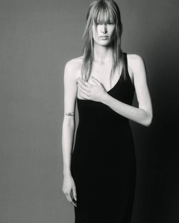 Monochrome portrait of a female model with bangs wearing a black dress against a plain grey studio backdrop.