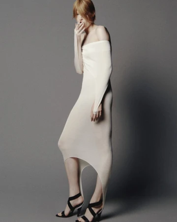 Model in long off-white dress holding cigarette against a plain grey backdrop