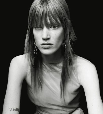 Monochrome portrait of a model with straight bangs and dark dangling earrings against a solid black background.