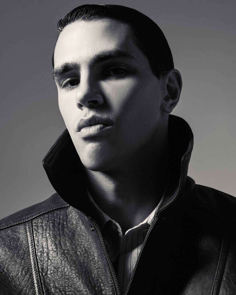 Portrait of a man wearing a dark high-collared jacket against a neutral studio backdrop.