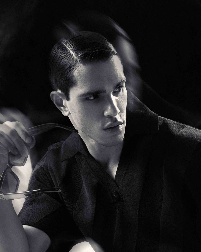 Black and white portrait of a man in a dark collared shirt holding glasses, for Glamour Man Bulgaria by Dan-Cristian Gocan.