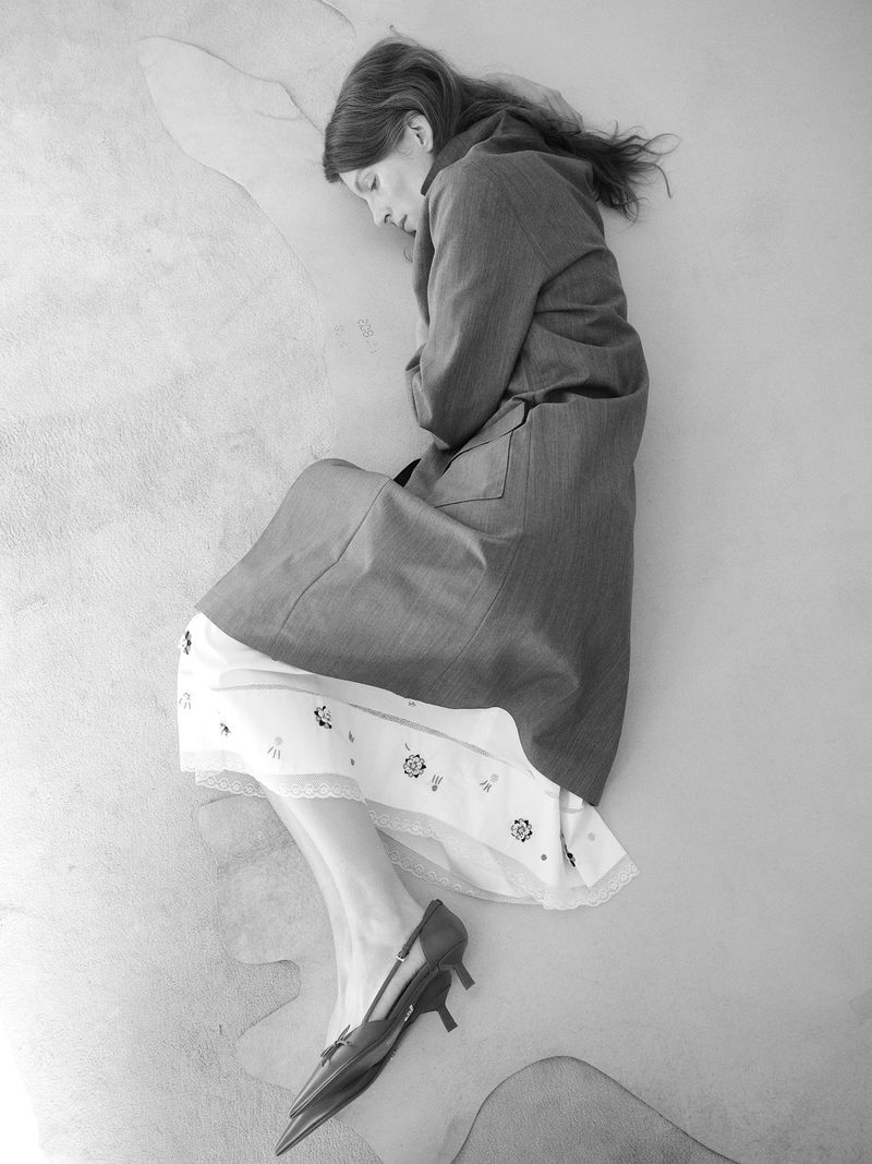 Model lying on a textured surface wearing a long coat and kitten heels for Family Style Unconditional project.