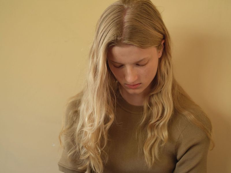 Portrait of a blonde woman looking downward against a warm solid background for Family Style