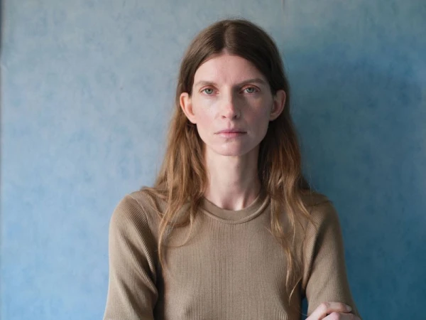 Portrait of a woman wearing a brown crewneck top against a mottled blue textured wall background