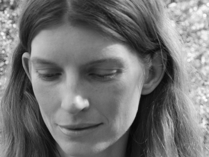 Close-up monochrome portrait of a woman looking downward against a soft blurred natural background